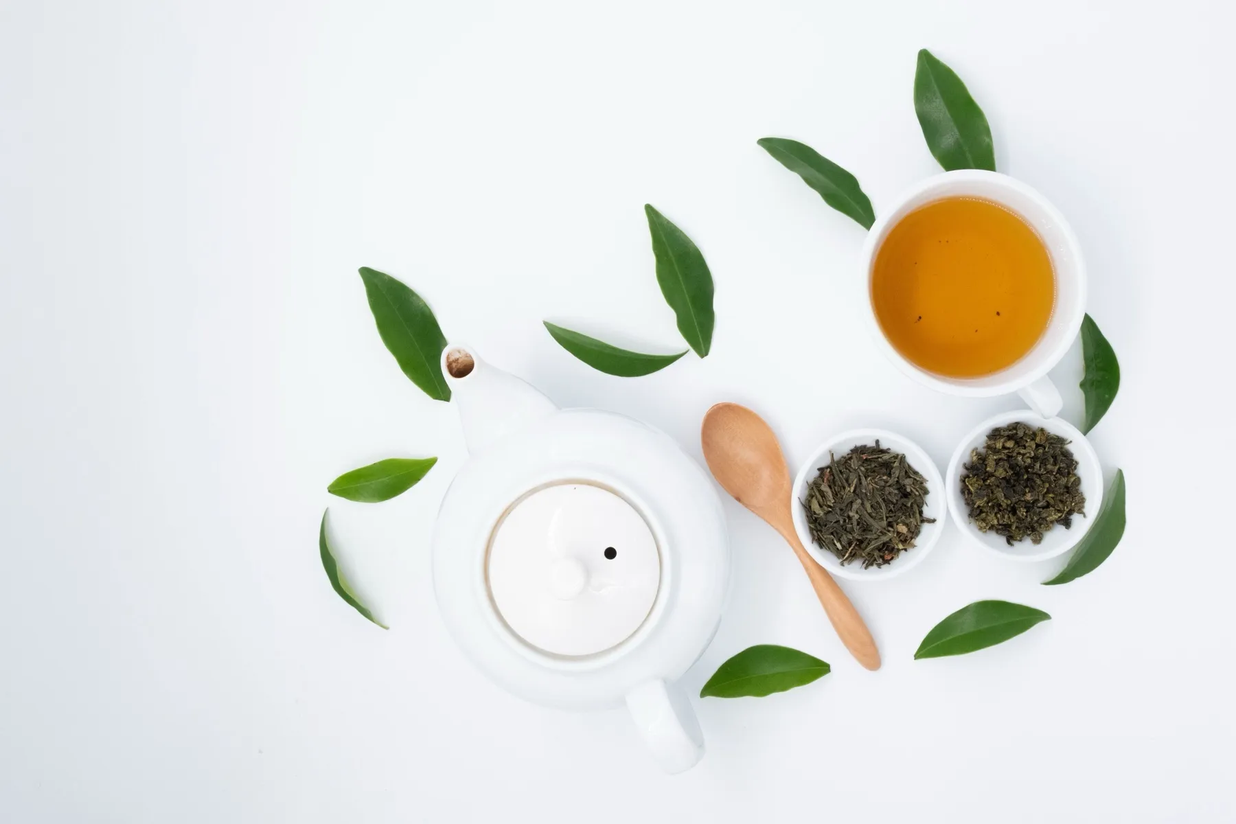 Green tea leaves beside a teapot.