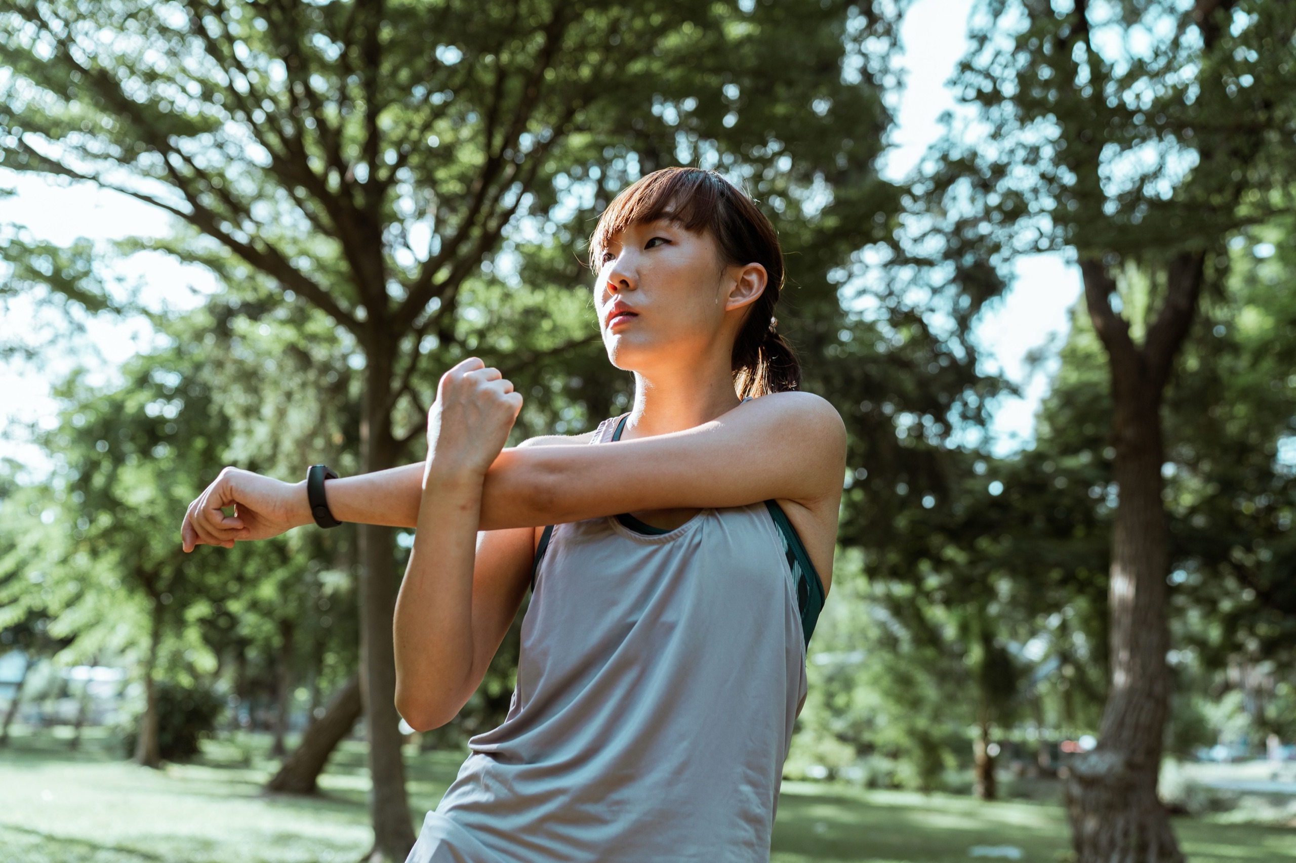 A woman stretching in a sunlit park before a morning run.